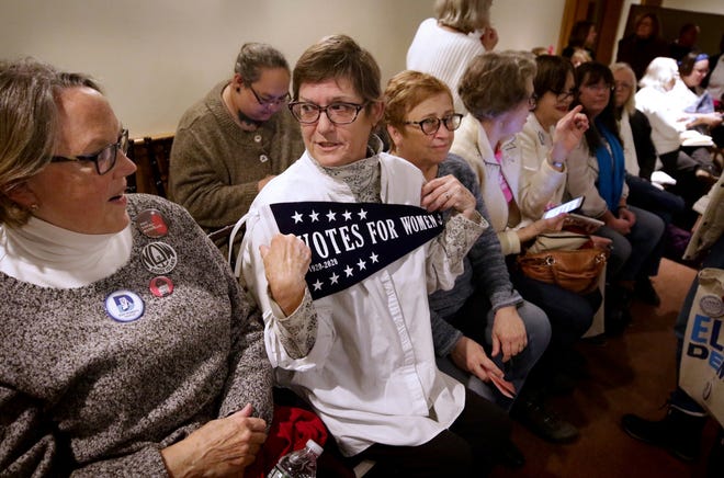 Susan Razza, of Newport, shows a pennant marking the 100th anniversary of women's right to vote to fellow Women's Caucus member Gail Harvey, left, of Cranston, during Monday night's meeting of the Rhode Island Democratic State Committee in Cranston. [The Providence Journal / Kris Craig]