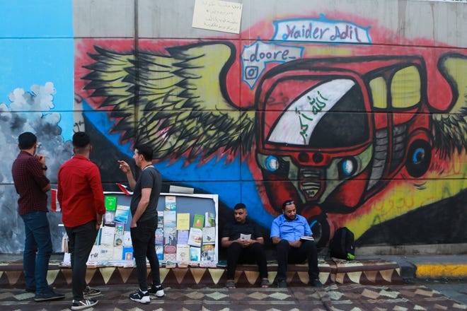 Protesters read donated books Sunday in front of graffiti, at the Saadoun Tunnel, in Baghdad, Iraq. The tunnel that passes under Baghdad’s landmark Tahrir Square has become an ad hoc museum for Iraq's revolution: Young artists draw images and murals that illustrate the country’s tortured past, and the Iraq they aspire to. [HADI MIZBAN/THE ASSOCIATED PRESS]