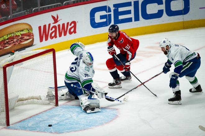 Washington Capitals center Evgeny Kuznetsov (92), from Russia, shoots the puck as Vancouver Canucks goaltender Jacob Markstrom (25) from Sweden, and defenseman Jordie Benn (4), from Canada, defend during the first period Saturday in Washington. [Al Drago/The Associated Press]