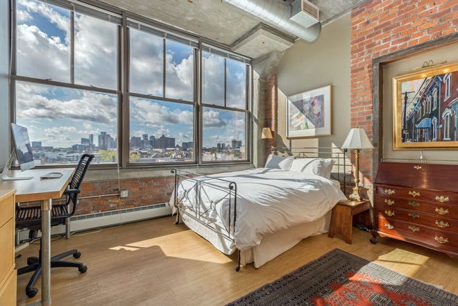 This three-windowed bedroom preserves an old brick-surrounded wood doorframe as a picture/dresser niche and exposes more exposed brick below the window-bank.