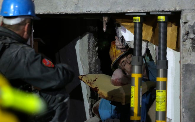 Rescuers try to free a man from a collapsed building after a magnitude 6.4 earthquake in Thumane, western Albania, on Tuesday. Rescue crews with excavators searched for survivors trapped in toppled apartment buildings and hotels Tuesday after a powerful pre-dawn earthquake in Albania killed at least 21 people and injured more than 600. [VISAR KRYEZIU/THE ASSOCIATED PRESS]