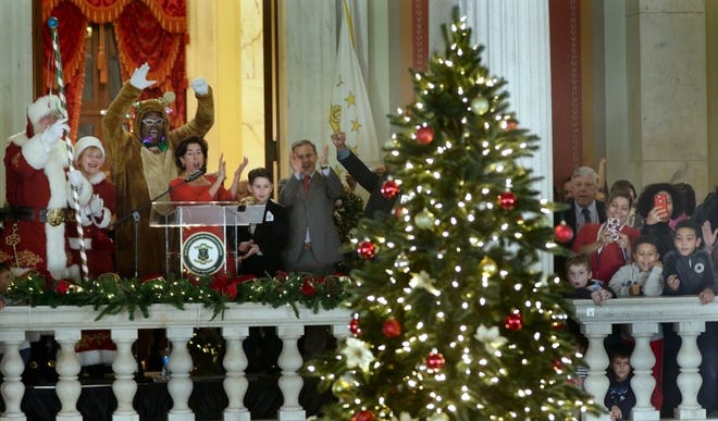 Governor Gina Raimondo; her husband, Andy Moffit, and their son, Tommy, celebrate the lighting of the state Christmas tree with help from Kasim Yarn (in the reindeer suit), state director of Veterans Affairs, on Wednesday in the State House. The state is displaying an artificial tree at the State House this year. [The Providence Journal / Kris Craig]