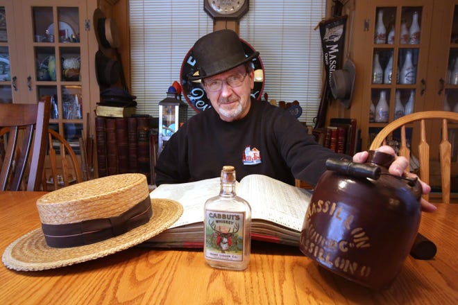 Local Massillon historian Rudy Turkal poses with some alcohol bottles from Massillon companies as well as some headwear from the Prohibition era. The book on the table is a 1932 Massillon Police log with the majority of arrests being noted as intoxication. 
(IndeOnline.com / Kevin Whitlock)