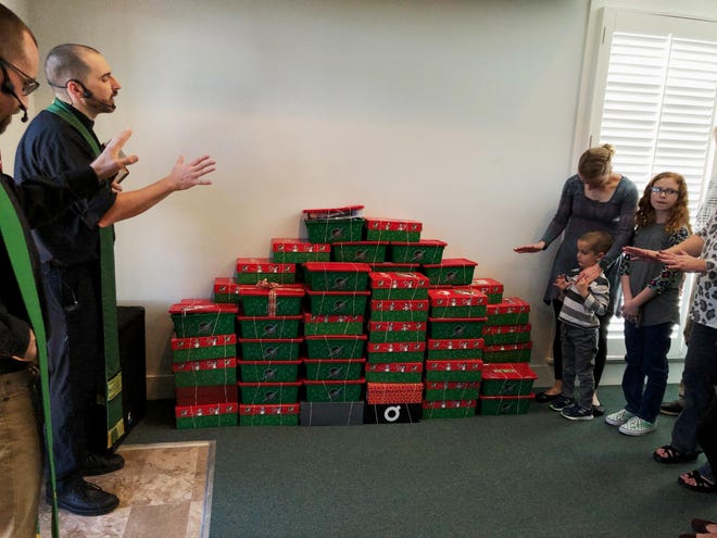 Father Caleb Miller and Father Ethan Harrison bless some of Immanuel Anglican Church's gift-filled Christmas shoe boxes before they were shipped to the district collection site in Crestview. Sonya Grant, Donna Schultz and Anne Fraser spent many hours collecting, organizing and transporting these boxes for the Destin community. Immanuel added a little over 100 boxes to the total of more than 10,000 that are beginning their journey to children around the world. [CONTRIBUTED PHOTO]