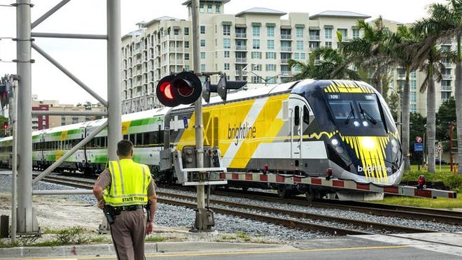 An off-duty FHP trooper blocks the Florida East Coast Railway crossings on Okeechobee Boulevard in downtown West Palm Beach as a Brightline train passes Thursday, July 13, 2017. Rail crossings throughout Florida will be upgraded for safety under a directive issued by the state transportation secretary. [Lannis Waters / The Palm Beach Post]