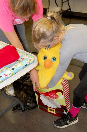 Kenna Huggard, 9, drops a stuffed animal into a gift bag with help from her mother, Kristen Huggard, at Sunday's Chamber gift-wrapping event at the Nickerson Community Center. Kenna has been waiting months to partcipate in the event and worked for hours wrapping presents. [John Green/Hutchnews]