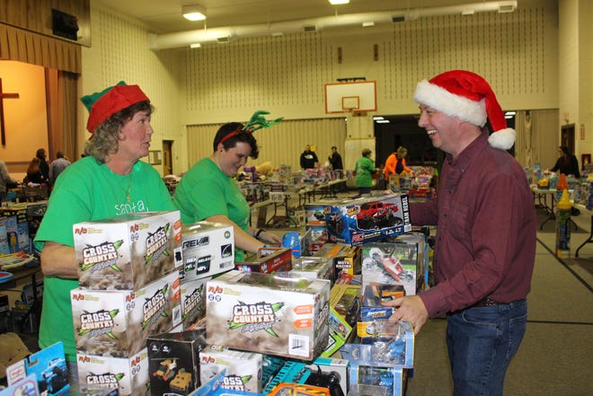 Beth Dale, left, and Colleen Walsh, center, help PVEN board president Tom Campbell stock a table of toys at Christ Hamilton Church in Sciota on Tuesday evening. PVEN, along with a number of churches and charitable organizations, held their annual toy program that provides families in need with a selection of free gifts on Tuesday and Wednesday. [BRIAN MYSZKOWSKI/POCONO RECORD]