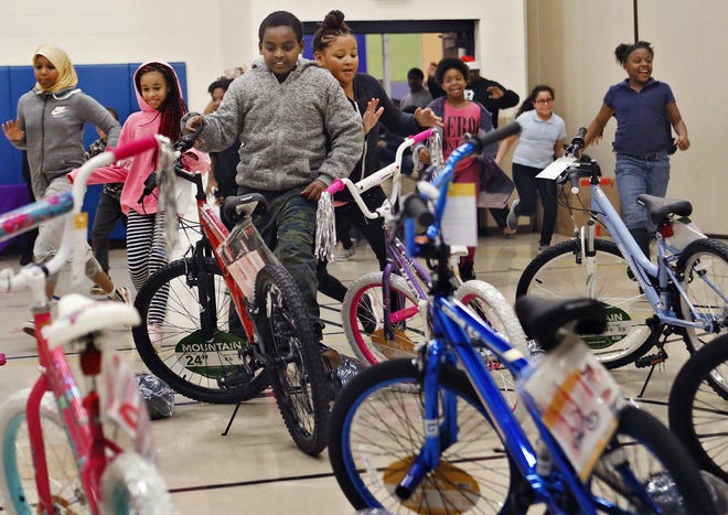 Ramadan Abubaker, 11, center, and Tiffany Carson, 11, bump shoulders while racing to get to their new bicycles at East Linden Elementary School on Friday. Ramadan said this was the first time he has owned his own bike. The bikes were donated to fifth-graders by New Salem Baptist Church Community of Caring Development Foundation; the helmets were provided by the Columbus Health Department. [Eric Albrecht/Dispatch]