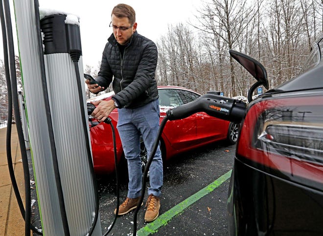 Andy Gottesman, 30, of Grandview Heights, prepares to hook up the Tesla Model 3 he bought in 2018 to a charging station at an office building near where he works for M/I Homes in the Easton area. “When I purchased it, I was able to get the tax credit, which helps make it a little more affordable as well,” he said. [Fred Squillante/Dispatch]