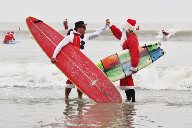 George Trosset Jr., left, and George Trosset high five each other during the 10th annual Surfing Santas event in Cocoa Beach, Fla., Tuesday. The event this year raised $40,000. [Malcolm Denemark/Florida Today]