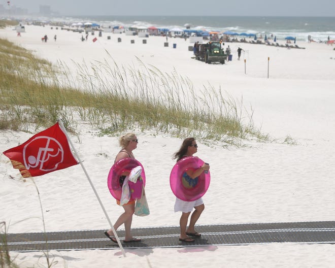 Beach-goers walk past a red flag cautioning against swimming near the M.B. Miller County Pier on Monday. [PATTI BLAKE/THE NEWS HERALD]