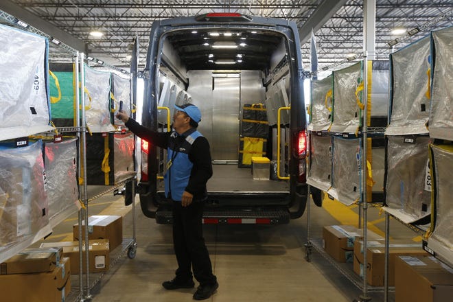 An Amazon driver checks stowed containers for delivery after robots separate packages by ZIP code at a warehouse in Goodyear, Ariz. Amazon and its rivals are increasingly requiring warehouse employees to get used to working with robots. [Ross D. Franklin/The Associated Press]