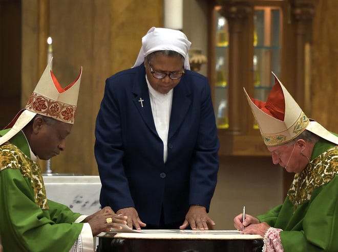 Cardinal Chibly Langlois, bishop of Les Cayes, Haiti, left, and Bishop Robert J. McManus, right, sign a document connecting the Diocese of Worcester and the Diocese of Les Cayes. Sister Marie Judith Dupuy directs the signing ceremony during Mass at St. Joseph Church Sunday, Sept. 3, 2017. [T&G File Photo/Rick Cinclair]