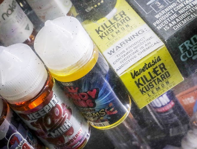 This Sept. 16, 2019, file photo shows flavored vaping solutions in a window display at a vape and smoke shop in New York. On Thursday, the Trump administration announced that it will prohibit fruit, candy, mint and dessert flavors from small, cartridge-based e-cigarettes that are popular with high school students. But menthol and tobacco-flavored e-cigarettes will be allowed to remain on the market. The flavor ban will also entirely exempt large, tank-based vaping devices, which are primarily sold in vape shops that cater to adult smokers. [BEBETO MATTHEWS/ASSOCIATED PRESS]