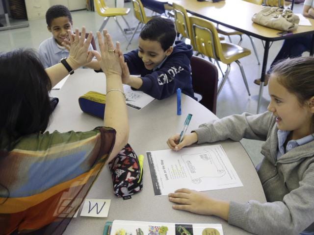 FILE PHOTO: In this April 3, 2013, photo, teacher Julia Puentes, left, high-fives student Mathew Botros, 9, center, during an English class at the Coral Way K-8 Center, the nation's oldest bilingual school, in Miami.