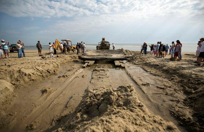 In this April 6, 2010, photo, volunteers and members of the North Carolina Wildlife Resources Commission use fire hoses, hand shovels and heavy equipment to remove the sand and pull what remains of a shipwreck off the beach in Corolla, N.C. Ships have struck the shoals off the coast for centuries, giving the area the nickname Graveyard of the Atlantic. (L. Todd Spencer/The Virginian-Pilot via AP)
