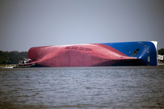 FILE - In this Sept. 9, 2019, file photo, a Moran tugboat nears the stern of the capsizing vessel Golden Ray as a tent and rescuers can be seen near the bottom of the ship near the tug boat in Jekyll Island, Ga. A Texas-based salvage company will cut up and remove the 656-foot (200- meter) shipwreck from St. Simons Sound off the coast of Georgia. The Coast Guard's Unified Command has hired T&T Salvage LLC of Galveston to remove the Golden Ray cargo ship, The Brunswick News reported. The ship, roughly the size of a 70-story office building, has sat overturned in the sound for four months. (AP Photo/Stephen B. Morton, File)