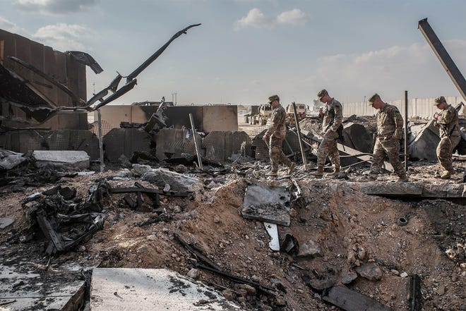 U.S. officials stand near a crater caused by Iranian airstrikes inside the Ain al-Asad base near Anbar, Iraq, on Monday. [EMILIENNE MALFATTO/THE WASHINGTON POST]