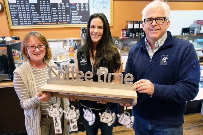 Colleen Snyder of the Portsmouth Hanging Coffee initiative, at left, holds the extra cup of coffee rack with Port City Coffee Roasters manager Donna Wilford, and owner Derek LaBorie. A paying customer can purchase an extra coffee at the register and a tag will be place on the rack for someone who is in need of one and unable to afford it. [Rich Beauchesne/Seacoastonline]