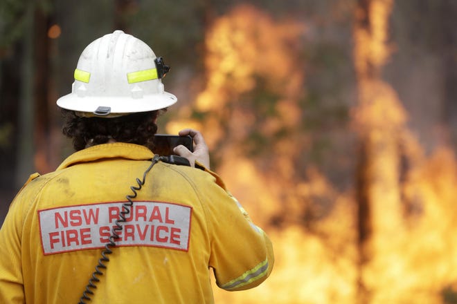A firefighter uses his phone to record a controlled burn near Tomerong, Australia, Wednesday, Jan. 8, 2020, in an effort to contain a larger fire nearby. Around 2,300 firefighters in New South Wales state were making the most of relatively benign conditions by frantically consolidating containment lines around more than 110 blazes and patrolling for lightning strikes, state Rural Fire Service Commissioner Shane Fitzsimmons said. (AP Photo/Rick Rycroft)