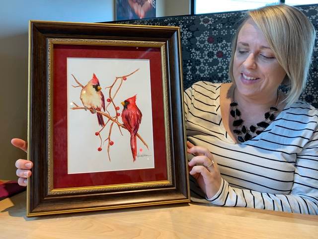 Gina Kahler holds up a portrait of two cardinals she painted. She attributes this painting for getting initial interest in her art and eventually starting her business. Photo by David Mullen/Ames Tribune