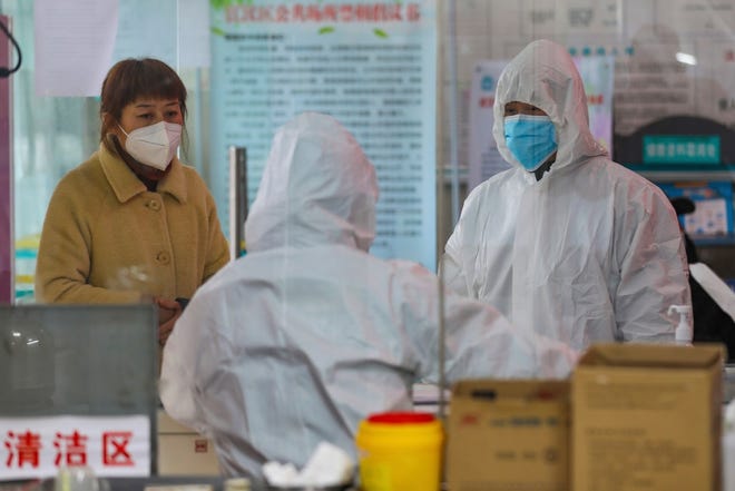 Medical workers in protective gear talk with a woman suspected of being ill with a coronavirus at a community health station in Wuhan in central China's Hubei Province, Monday. [THE ASSOCIATED PRESS]