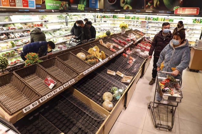 FILE - In this Jan. 25, 2020 photo, shoppers wearing face masks look for groceries near mostly empty produce shelves at a supermarket in Wuhan in central China's Hubei province, Saturday, Jan. 25, 2020. Complicated logistics are part of a daily flow of food and other goods authorities say is sustaining Wuhan and surrounding cities with a total of 50 million people. Most are blocked from leaving in the most sweeping disease-control measures ever imposed. (Chinatopix via AP, File)
