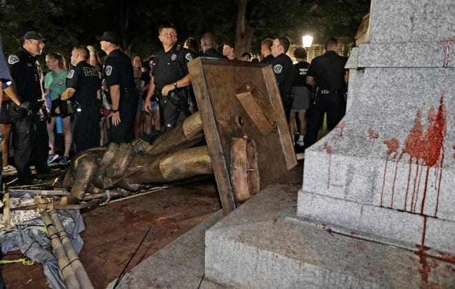 In this Aug. 20, 2018 file photo, police stand guard after the confederate statue known as Silent Sam was toppled by protesters on campus at the University of North Carolina in Chapel Hill, N.C.  Judge Allen Baddour ruled Wednesday, Feb. 12, 2020 that the Sons of Confederate Veterans didn’t have standing to bring the lawsuit that led to the hastily arranged deal that gave them possession of the statue known as Silent Sam, along with $2.5 million to maintain it. He vacated the deal and also dismissed the underlying lawsuit brought by the SCV. Critics had questioned how the deal was quietly struck with the UNC Board of Governors and approved just before Thanksgiving. [AP Photo/Gerry Broome, File]