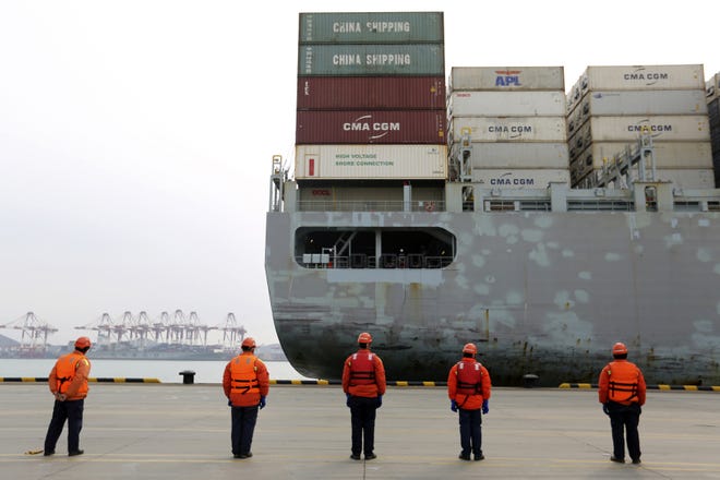 Workers watch a container ship arrive at a port in Qingdao in east China's Shandong province. Factories across China are still closed to try to limit spread of the coronavirus, leaving business owners in limbo. [Chinatopix via AP]