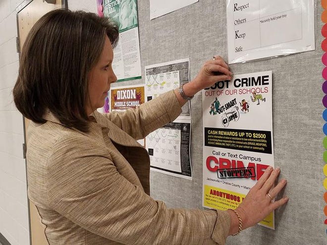 Dixon Middle School Principal Leigh Bizzell posts a Crime Stoppers poster on one of the school bulletin boards to help keep students aware of the program. [Jannette Pippin / The Daily News]