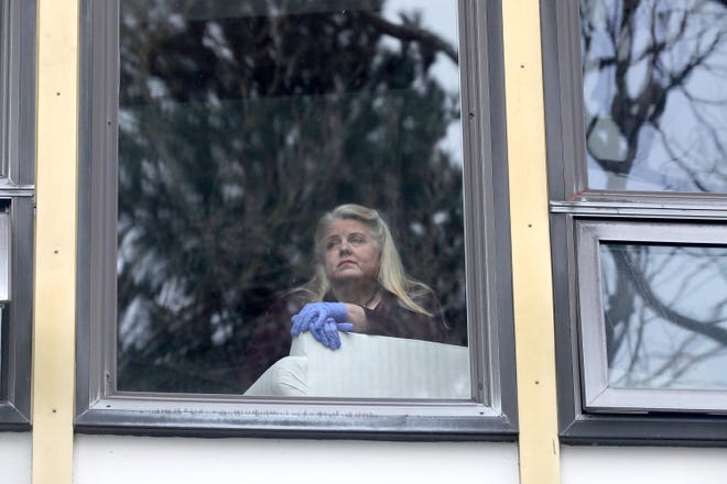Wearing rubber gloves, retired choir director Carleigh Bedell is self-isolating due to concerns about COVID-19 and because she is at higher risk due to underlying health conditions. She peers out her second floor apartment window. (Greg Gilbert/The Seattle Times/TNS)