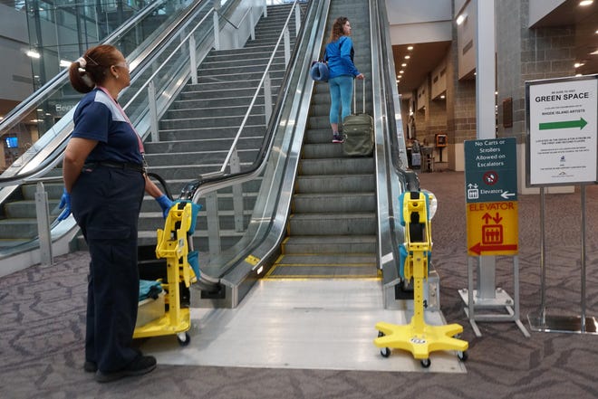 A traveler ascends the escalator at T.F. Green Airport in Warwick as housekeeper Josephina Franco attends to the machines that clean the handrails. The machines are rotated to clean all the handrails in the airport. [The Providence Journal / Sandor Bodo]