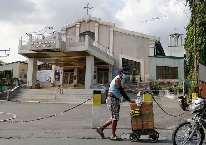A vendor wearing a protective mask walks past a church in suburban Quezon city, in Manila, Philipines on Saturday March 14, 2020. Masses at churches in metropolitan Manila have been suspended as a precautionary measure against the spread of the new Coronavirus. Philippine officials on Saturday declared a night curfew in the capital and said millions of people in the densely populated region could only go out of their homes for work, buy necessities and medical emergencies at daytime under a monthlong quarantine to be imposed to fight the new coronavirus.
