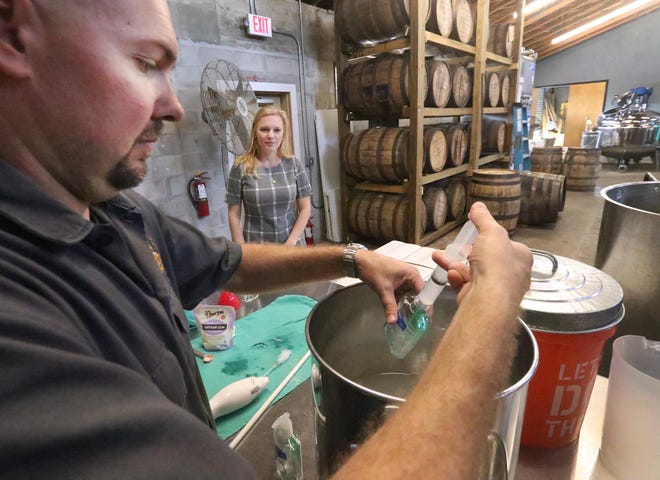 Copper Bottom Craft Distillery owner Jeremy Craig fills a small bottle with hand sanitizer while his wife and co-owner Jenni Craig looks on, Wednesday March 18, 2020 as the Holly Hill distillers use some of their product to make hand sanitizer and give it away to those in the community during the Coronavirus outbreak.  [News-Journal/David Tucker]