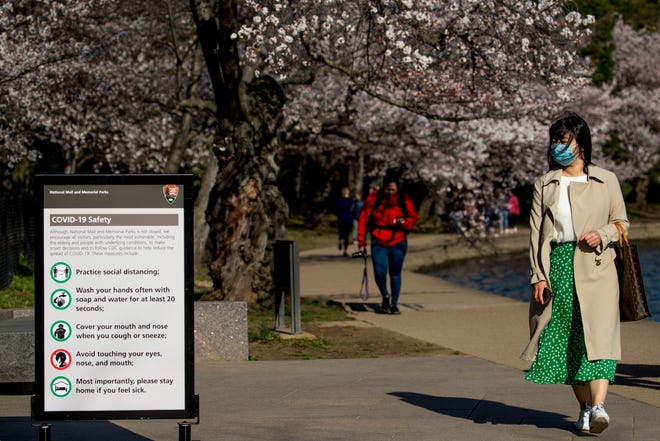 A woman wearing a mask stops to read coronavirus safety tips along an almost empty Tidal Basin lined with cherry blossoms that are about to peak, Wednesday, March 18, 2020, in Washington. (AP Photo/Andrew Harnik)
