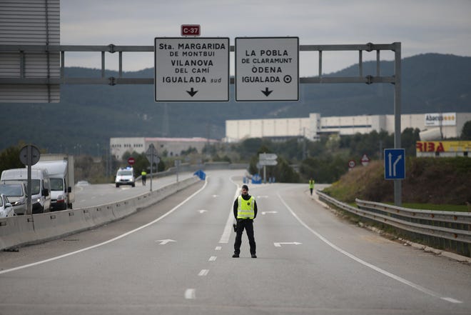 A mosso de esquadra police officer stands on the closed-off road near Igualada, Spain, on March 13. More than 60,000 people awoke Friday in four towns near Barcelona confined to their homes and with police blocking roads. A number of U.S. states have now issued stay-at-home orders that mirror the lockdowns seen in Spain and elsewhere, and pressure is building on Florida Gov. Ron DeSantis to consider something similar. [Joan Mateu/ Associated Press Photo]