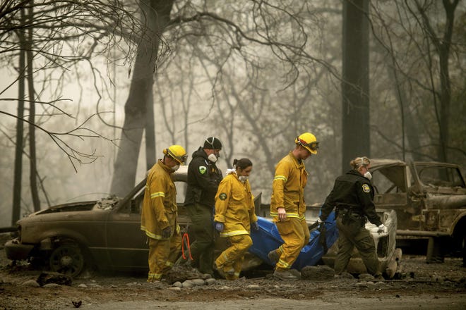 Firefighters and deputies carry the body of a Camp Fire victim in Paradise in 2018. Pacific Gas & Electric has agreed to plead guilty to 84 counts of involuntary manslaughter in connection with the Camp Fire, which killed 84 people and decimated three towns. [NOAH BERGER/AP FILE 2018]