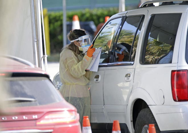 A Healthcare worker helps to check in as vehicles line up at the COVID-19 drive-thru testing center at Marlins Park as the coronavirus pandemic continues on Wednesday in Miami. [David Santiago/Miami Herald]