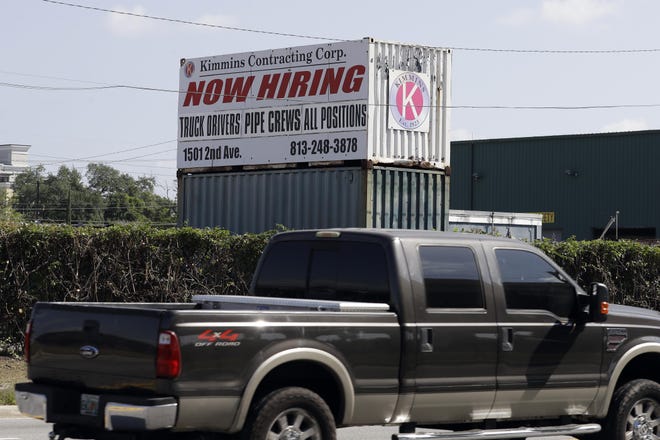 Drivers pass a sign outside the Kimmins Contracting Corp., looking to hire employees Thursday in Tampa. A record-high number of people applied for unemployment benefits last week as layoffs engulfed the United States in the face of a near-total economic shutdown caused by the coronavirus. [Chris O'Meara/The Associated Press]