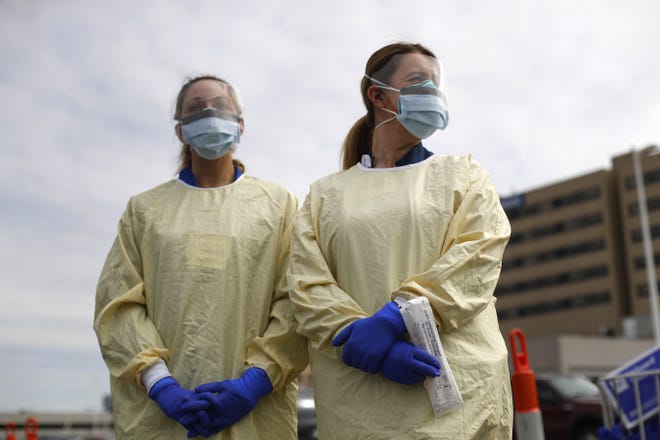 Physicians Assistant Jessica Hamilton, left, and Amena Beslic RN holds a swab and test tube kit to test people for COVID-19 at a drive-thru station set up in the parking lot of the Beaumont Hospital in Royal Oak, Mich., Monday, March 16, 2020. (AP Photo/Paul Sancya)