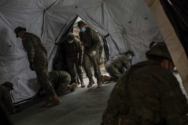 Spanish Army soldiers mount a tent to be used by hospital patients during the coronavirus outbreak in Madrid, Spain, Monday, March 30. Bells tolled in Madrid's deserted central square and flags were lowered in a day of mourning Monday as Spain raced to build field hospitals to treat an onslaught of coronavirus patients. (AP Photo/Bernat Armangue)