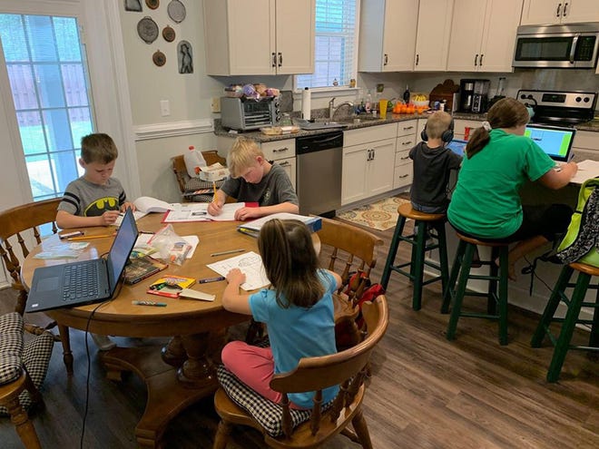 One mother has shifted to working from home and is, all-of-a-sudden, teaching five children at home. She says she’s lucky that two of them got Chromebooks for Christmas and the family has enough tablets and computers for them all. Seated at the table, in the Batman shirt, is Royce White, 6. Next to him at the table is Reed Hatch, 10. Also at the table is Ellanore Woods, 4. At the counter with headphones is E.B. White, 4. To his right, at the counter, is Zayleigh Howell, 11. [COURTESY HILARY WOODS]
