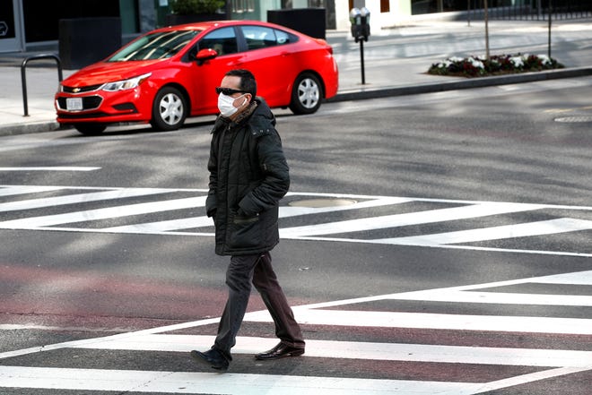 A man wearing a face mask crosses a street, Wednesday, April 1, 2020, in Washington. The District of Columbia has issued a stay-home order for all residents as the number of positive infections from the new coronavirus continue to rise. (AP Photo/Patrick Semansky)