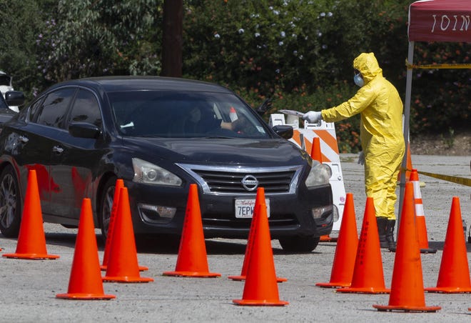 Los Angeles Fire Department officials deliver testing kits to a waiting motorists at a COVID-19 drive-up testing site in Elysian Park on Thursday. Officials say hand-washing and keeping a safe social distance are priorities in battling the COVID-19 virus. [DAMIAN DOVARGANES/AP]