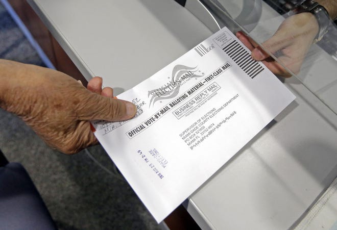 In 2016, a voter hands his absentee ballot to a Miami-Dade County elections official. [AP Photo/Alan Diaz]