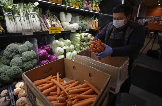 A worker, wearing a protective mask and gloves against the COVID-19 coronavirus, stocks produce before the opening of Gus's Community Market on Friday in San Francisco. Health experts say there's no evidence the new coronavirus is spread through food. [AP Photo/Ben Margot]