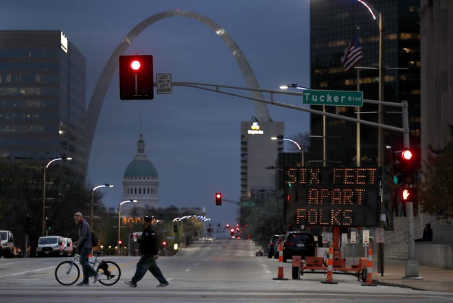 People cross a street near a sign encouraging social distancing Thursday in St. Louis. The city is under a stay-at-home order asking residents to stay inside and away from others as much as possible in an effort to slow the spread of the coronavirus. [Jeff Roberson/The Associated Press]