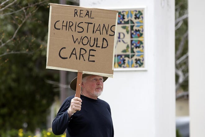Andrew Goetze holds a sign in opposition to a Palm Sunday service taking place at Godspeak Calvary Chapel in Newbury Park. Many churches, beaches, parks and hiking trails around the state have been closed because they attracted large crowds amid the coronavirus outbreak. [MARCIO JOSE SANCHEZ/THE ASSOCIATED PRESS]