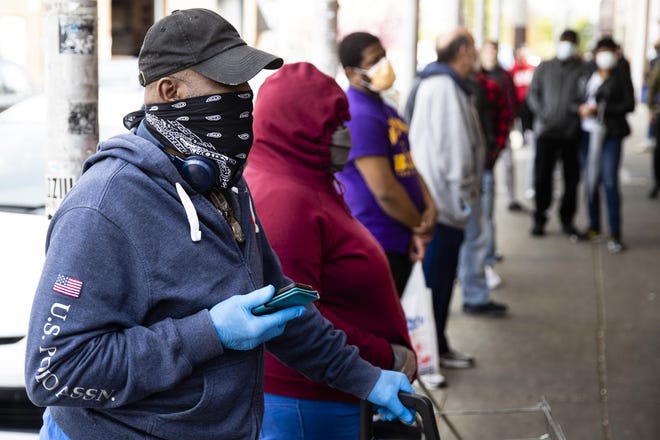 George Ricketts, wearing a face covering to protect against the spread of the new coronavirus, waits to enter a store on South 9th Street in the Italian Market neighborhood of Philadelphia on Thursday. [AP Photo/Matt Rourke]
