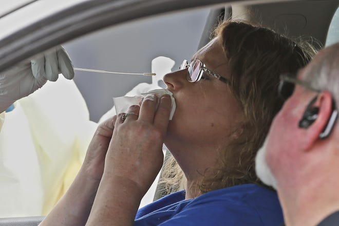 A woman in the passenger seat of a car is swabbed for a COVID-19 test at a mobile testing site run by the Cleveland County Health Department Thursday, April 9, 2020, in Norman, Okla. The new coronavirus causes mild or moderate symptoms for most people, but for some, especially older adults and people with existing health problems, it can cause more severe illness or death. (AP Photo/Sue Ogrocki)